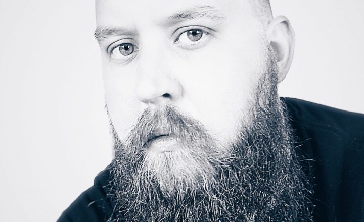 portrait of John Wayne Hill, a San Francisco Product Designer, in black and white; a man with medium hair and shaved sides with a long beard wearing a black t-shirt